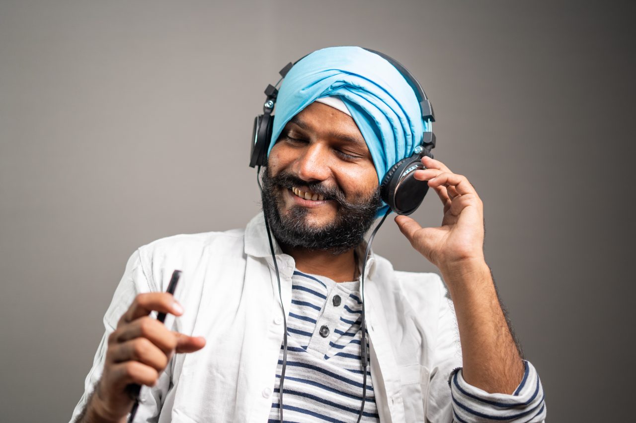 Smilende, ung sikh med turban lytter til musikk med øreklokker på.