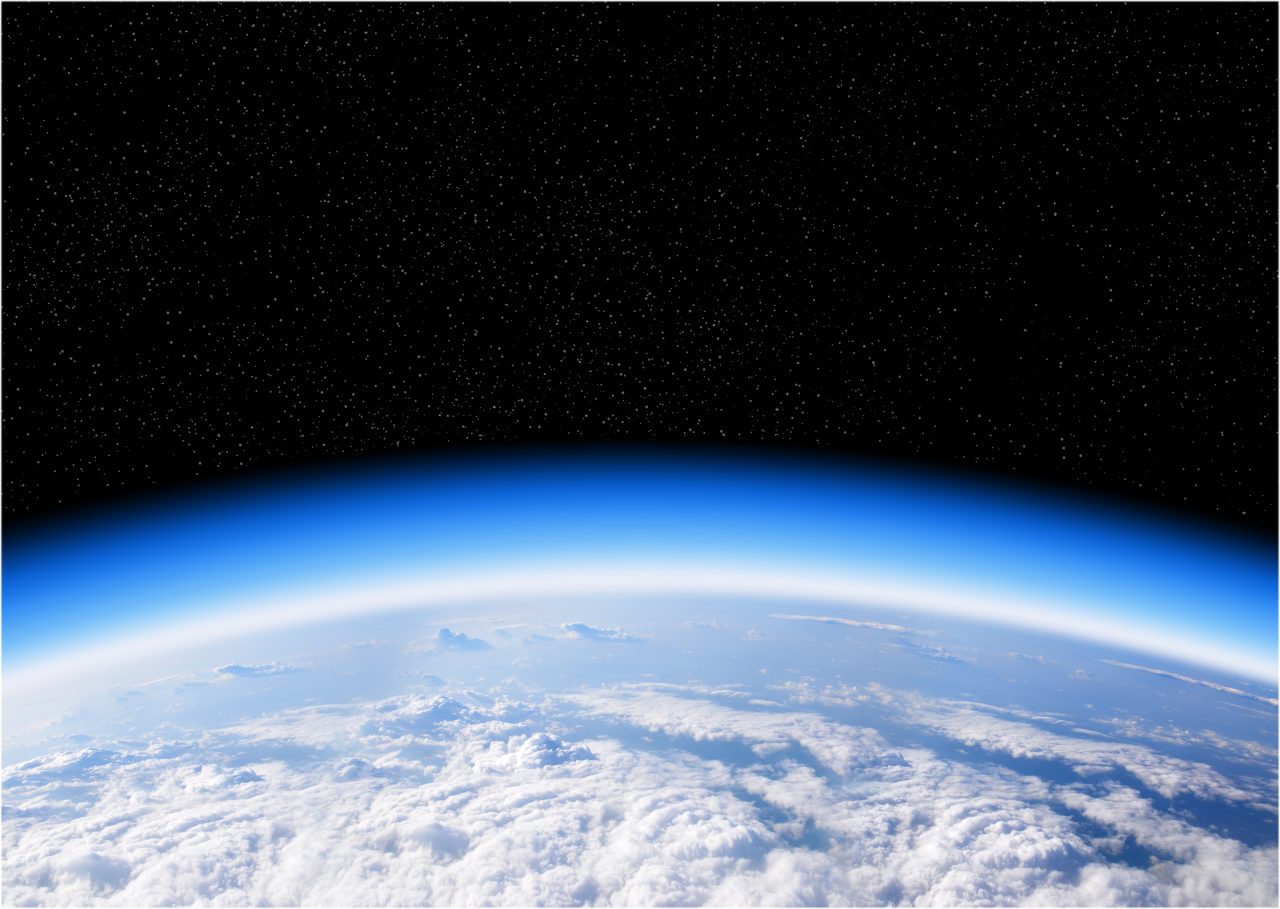 Utsikt mot jorda sett fra verdensrommet, med blå atmosfære, skyer og mørkt stjernehimmel bak.